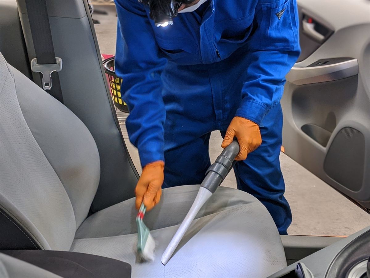 ブラシと掃除機で車のシートを清掃する作業スタッフ(車内清掃の基本作業)